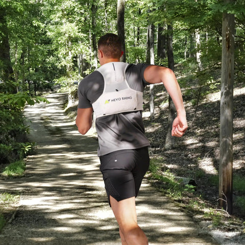 Back view of a man running with ultralight running hydration vest with two 500ml TPU soft flasks on forest trail.