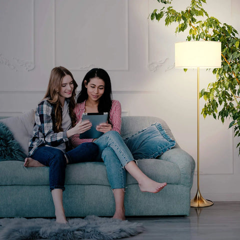 Cozy living room scene with Quinn LED Floor Lamp With Drum Shade Sleek Modern Standing Light For Living Rooms Offices And Bedrooms Mid Century Design With Heavy Base For Stability Brass Gold Finish Dope Decor And Reading Lamp beside a sofa.