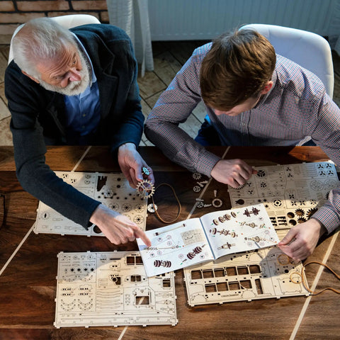 Two people assembling Steampunk 3D Puzzle Clock Kit For Adults With 378 Pieces Including 43 Spare Parts, using colorful instructions.