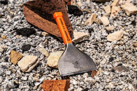 Brick Chisel 4 Inch By 7 And A Half Inch With Enlarged Striking Cap High Visibility Rawhide Paint Bold Size Markings Heat Treated Steel Rust Resistant Lacquer Finish ASME Tested To 150 Percent For Heavy Duty Masonry on gravel surface