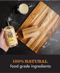 Hand holding Cutting Board Oil With Lemon And Orange Oils Food Grade Mineral Oil For Cutting Boards And All Wood Surfaces Keeps Your Boards Looking Fresh Restores And Protects Butcher Block Nourishing Conditioner 12 Oz bottle next to cutting board and conditioner jar.