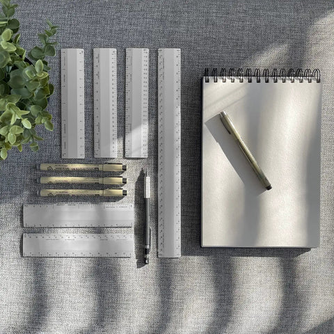 Metal Architect Ruler 12 Inch Pro Grade With Four Bevel Scales For Drawing Drafting And Engineering Left To Right Calibrations One Thirty Second One Sixteenth One Eighth And One Quarter For Precise Measurements. Metal drafting rulers, notepad, and pen on desk