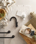 Flat lay with Doux Matte Black 24-Inch Single Towel Bar for Bath and Kitchen, faucet, and decor items on linen and wood surface.