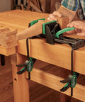 Rock Solid 6 Inch Quick Action Bench Vise With 300 Pound Clamping Power holding wooden piece on workbench with rubber jaws.