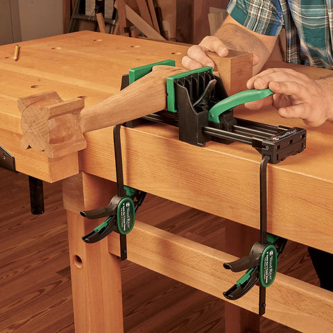 Rock Solid 6 Inch Quick Action Bench Vise With 300 Pound Clamping Power holding wooden piece on workbench with rubber jaws.