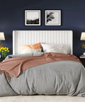 White Queen Velvet Bed Frame With Upholstered Wingback Headboard And Vertical Tufted Design Built On Heavy Duty Metal Base With Wooden Slats For Quick No Box Spring Bedroom Setup That Brings Major Style And Hits Different with gray bedding and decorative pillows.