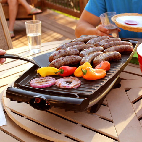 Indoor Outdoor Electric Grill With Nonstick Griddle Plate And Fat Reduction Drip Tray Twelve Plus Servings On A 200 Square Inch Surface Portable Apartment Friendly Barbecue For Easy Weekend Grilling in use with sausages and vegetables
