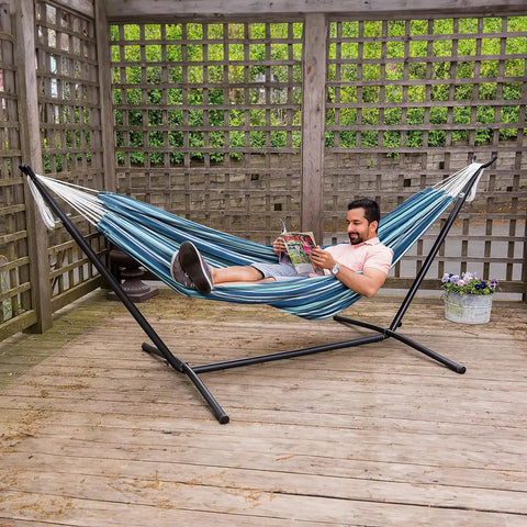 Man relaxing in Two Person Outdoor Hammock With Adjustable Metal Stand For Patio Or Garden, space saving Brazilian style, blue stripe