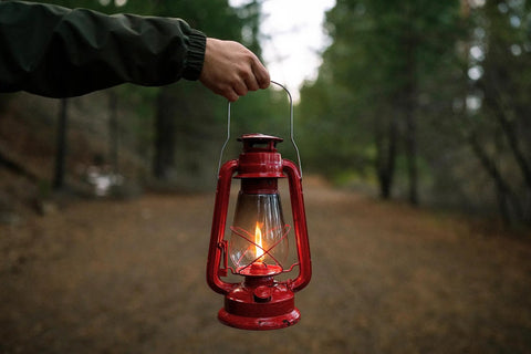 12 Inch Hurricane Lantern With Durable Red Finish For Camping And Emergencies held outdoors on a forest path.