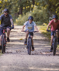 Flatrock DX Mountain Bike With 29 Inch Wheels 21 Speed Drivetrain Aluminum Frame Front Suspension Twist Shifters And Mechanical Disc Brakes Built Tough For Adult Men And Women On Rugged Trails on forest path with riders.