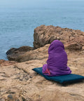 Person in an Ultralight Camping Sleeping Bag For Adults And Kids on rocky coastline, focused on sleeping bag features.