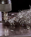 Close-up of a 5/8 in annular cutter mounted in a knurled drill chuck with metal shavings on a steel surface.