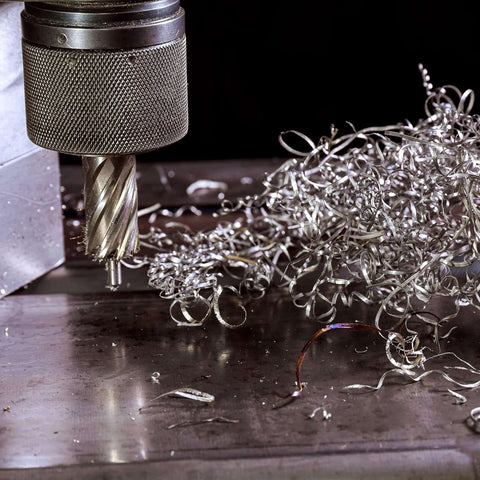 Close-up of a 5/8 in annular cutter mounted in a knurled drill chuck with metal shavings on a steel surface.