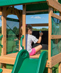 Child drawing on chalkboard in Buckley Hill Cedar Wood Swing Set With Wave Slide, Elevated Play Deck, Canopy Roof, Outdoor Backyard Playset.