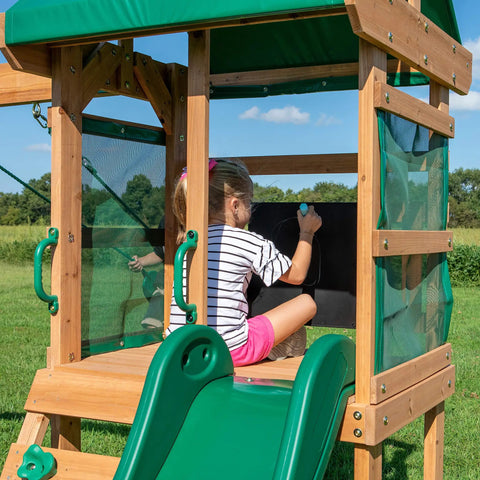Child drawing on chalkboard in Buckley Hill Cedar Wood Swing Set With Wave Slide, Elevated Play Deck, Canopy Roof, Outdoor Backyard Playset.
