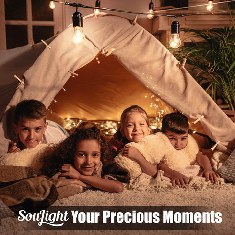 Four children smiling inside a cozy tent with hanging lights in a warmly lit room