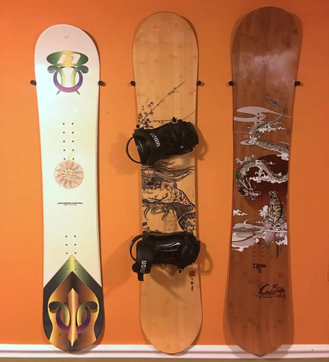 Minimalist Snowboard Wall Mount Display Rack Featuring Felt Padded Arms And Durable Rubber Grip To Stash Your Sick Ride Securely In Garage Or Home Studio And Recreation Room - three snowboards mounted on orange wall.