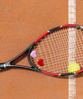 Heart Shaped Tennis Dampeners Set Of 4 Silicone Vibration Absorbers in red and pink on a racket near a tennis ball on clay court