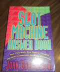 Fourth Edition Slot Machine Handbook By John Grochowski on a wooden table, colorful paperback cover, casino gaming guide.