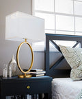 Oke Table Lamp With Gold Plated Finish, Modern Art Deco Open Round Frame, White Rectangular Shade on a nightstand.