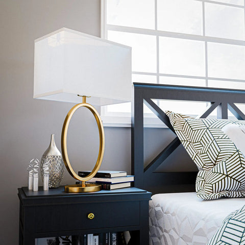 Oke Table Lamp With Gold Plated Finish, Modern Art Deco Open Round Frame, White Rectangular Shade on a nightstand.