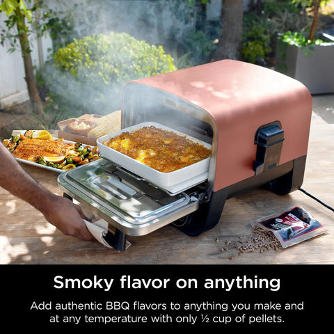 Woodfire Outdoor Pizza Oven 8 In 1 Portable Electric Roaster Heats Up To 700 Degrees Fahrenheit, Terracotta Red, on a patio table in use.