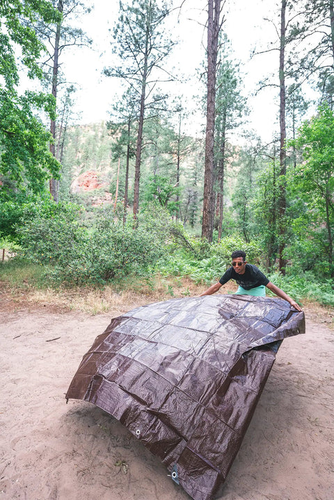 Person setting up Rip Stop Tarp 8 By 10 Feet Heavy Duty Waterproof Brown Outdoor Shelter For Camping And Backyard Use in a forest