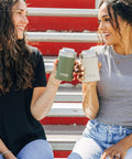 Two women holding Heavy Duty 12 Oz Can Cooler With Tight Seal Lid Double Wall Vacuum Insulated Stainless Steel Chiller Keeps Beer And Soda Bangin Cold Zero Sweat Build Olive.