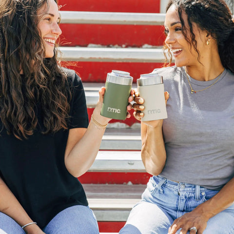 Two women holding Heavy Duty 12 Oz Can Cooler With Tight Seal Lid Double Wall Vacuum Insulated Stainless Steel Chiller Keeps Beer And Soda Bangin Cold Zero Sweat Build Olive.