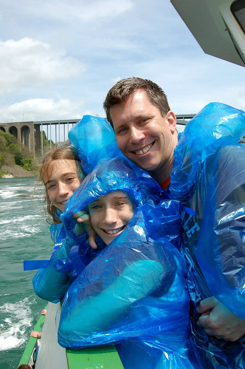 Family wearing blue ponchos outdoors, highlighting Extra Thick Family Rain Ponchos 8 Pack For Men Women Teens And Kids Disposable Emergency Rain Gear With Drawstrings Durable Waterproof Ponchos For Travel And Disney Trips Stay Dry On The Go in use.