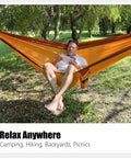 Person relaxing in an orange Double Camping Hammock With Tree Hanging Kit And 12Kn Aluminum Wiregate Carabiner Parachute Nylon.