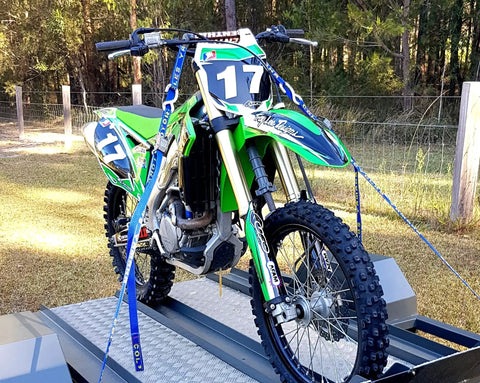 Adjustable Motorbike Fork Stand Heavy Duty Dirt Bike Transport Rack stabilizing a dirt bike in a trailer with blue tie-down straps.