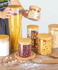 Airtight Glass Storage Jars Set Of 7 With Bamboo Lids For Pasta Cookies Nuts Coffee Beans Cereal Flour Pantry Organization BPA Free Clear Glass Canisters displayed on a table with various foods.