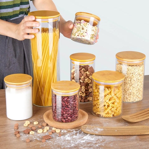 Airtight Glass Storage Jars Set Of 7 With Bamboo Lids For Pasta Cookies Nuts Coffee Beans Cereal Flour Pantry Organization BPA Free Clear Glass Canisters displayed on a table with various foods.