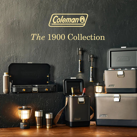 The Coleman 1900 Collection featuring camping gear with grill, coolers, and lantern on wooden surface.