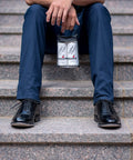 Person sitting on stairs holding Premium Leather Cleaner And Conditioner Kit with polished black shoes.