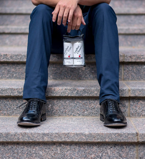 Person sitting on stairs holding Premium Leather Cleaner And Conditioner Kit with polished black shoes.