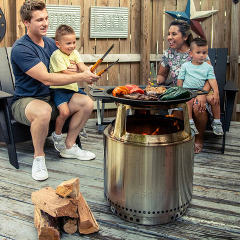 Family gathered around Bonfire Hub Stainless Steel Cooking Adapter For 8 Inch Elevation Fire Pit with food on grill.