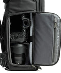 Side view of Roll Top 30L Camera Backpack with open side access, showing camera and lens storage in Asphalt Black expandable travel bag.
