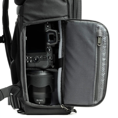 Side view of Roll Top 30L Camera Backpack with open side access, showing camera and lens storage in Asphalt Black expandable travel bag.