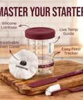 All In One Sourdough Starter Kit with glass jar, silicone lid, linen cover, temperature guide, and tools on a wooden board.
