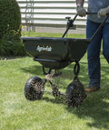 Person using 85 Lb Push Lawn And Garden Broadcast Spreader For Seed And Fertilizer, Walk Behind With Easy Cable Control on grass