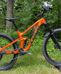 Orange mountain bike with Rear Derailleur Guard For Mountain Bikes And EBikes, Ultra Lightweight And Easy To Install, Universal Fit No Modifications Needed, Protect Your Derailleur From Rocks, Roots And Obstacles On The Trail Made In USA in a forest setting.
