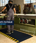 Industrial Anti Fatigue Mat For Standing Workstations with yellow border under worker at machinery in factory setting