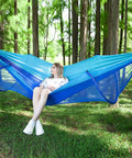 Woman relaxing in a blue Ultra Comfy Camping Hammock With Mosquito Net, 13ft tree straps, carabiners, in a forest setting