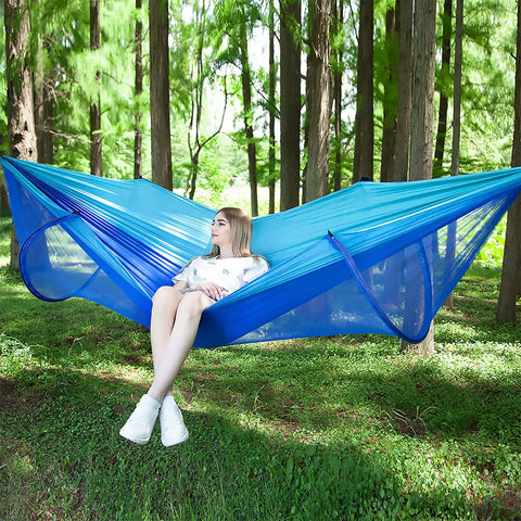Woman relaxing in a blue Ultra Comfy Camping Hammock With Mosquito Net, 13ft tree straps, carabiners, in a forest setting
