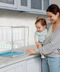 Woman with baby next to three tier clear acrylic baby bottle storage organizer for countertop or cabinet large capacity station