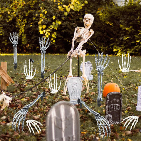 Outdoor Halloween scene with 18 Piece Realistic Skeleton Arm Stakes and Hands Set among tombstones and pumpkins on lawn.