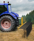 72 Inch Tow Behind Landscape Rake with 32 Steel Tine Dethatcher for Category 1 Tractors attached to a blue tractor on a field