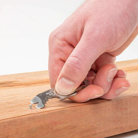 Hand using DoohicKey Keychain Multi Tool Stainless Steel 8 In 1 Bottle Opener Nail Puller Wrench on wooden surface